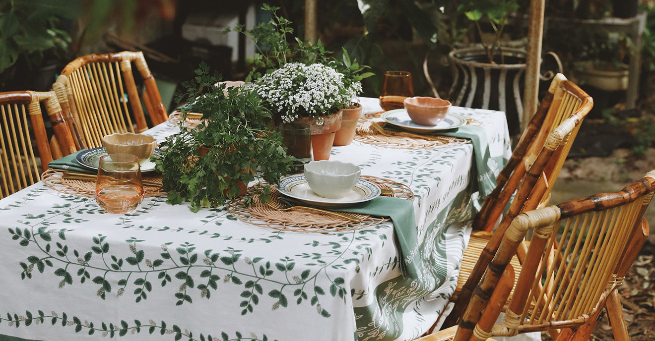 Dining table set with a floral tablecloth, chairs, and decorative items outdoors.